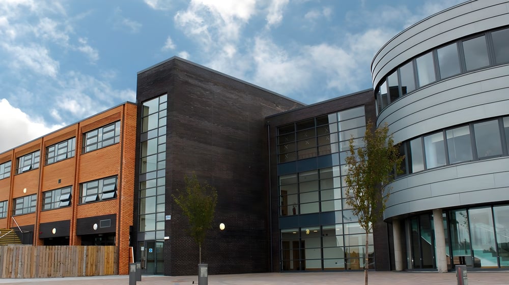 Das moderne mehrstöckige Gebäude der Assumption Grammar School mit einer Fassade aus Backstein, Glas und Holz vor bewölktem Himmel.