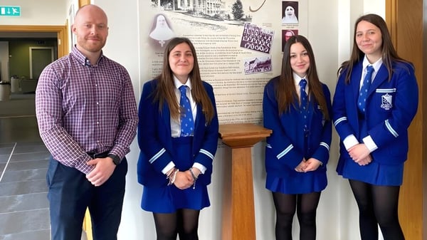 Eine Gruppe von Schülerinnen und Schülern steht im Flur der Assumption Grammar School vor einem Informationsbrett.