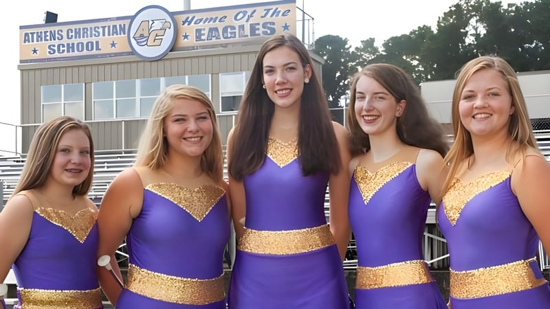 Fünf Schülerinnen in Cheerleading-Uniformen stehen vor einem Gebäude der Athens Christian School.