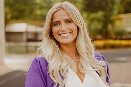 Eine Frau steht lächelnd vor einem unscharfen Außenbereich auf dem Campus der Athens Christian School.