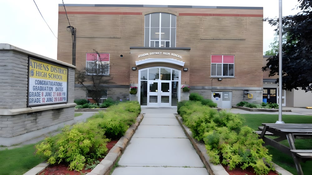 Das Backsteingebäude mit einem gewölbten Eingang auf dem Gelände der Athens District High School ist von gepflegtem Rasen und Bepflanzung umgeben.