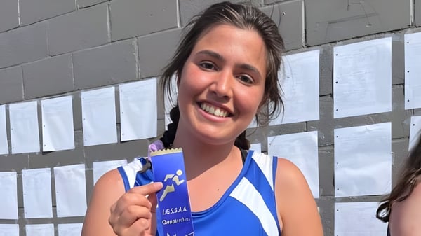 Eine junge Frau lächelt vor einer grauen Betonwand auf dem Campus der Athens District High School.