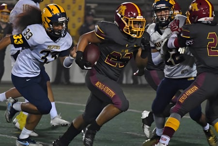 Die Footballmannschaft der Atherton State High School spielt zusammen, ein Spieler trägt den Ball während seine Teamkameraden ihn umgeben.