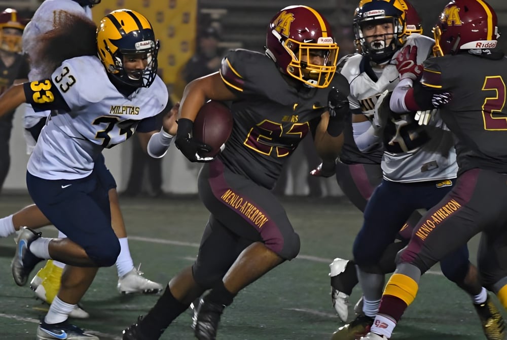 Die Footballmannschaft der Atherton State High School spielt zusammen, ein Spieler trägt den Ball während seine Teamkameraden ihn umgeben.