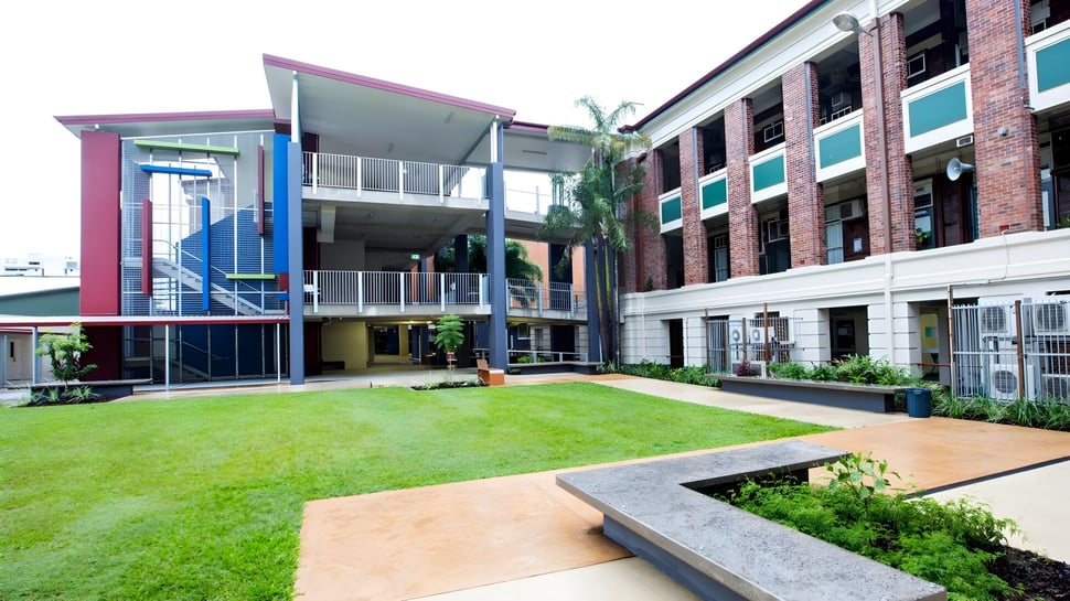 Das moderne bunte Gebäude der Atherton State High School mit einem grasbewachsenen Innenhof und einer Palme im Vordergrund.