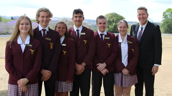 Eine Gruppe Schüler der Atherton State High School steht auf einem grasbewachsenen Feld vor Gebäuden und Bäumen.