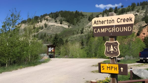 Ein Weg führt zu einem Campground-Schild in einer bewaldeten Gebirgslandschaft mit klarem Himmel nahe der Atherton State High School.