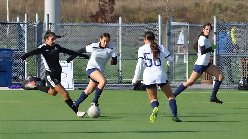 Eine Gruppe von Fußballspielerinnen trainiert auf dem Sportplatz des Athlete Institute vor einem Zaun und Gebäuden.