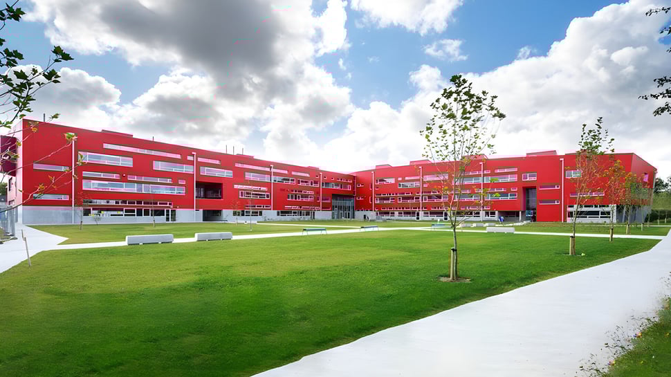 Das moderne rote Gebäude des Athlone Community College mit einem Rasen im Vordergrund unter bewölktem Himmel.