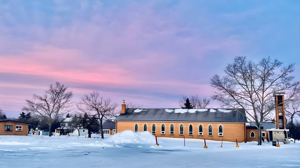 Das Athol Murray College of Notre Dame zeigt ein Backsteingebäude mit verschneitem Winterwald und buntem Himmel im Hintergrund.