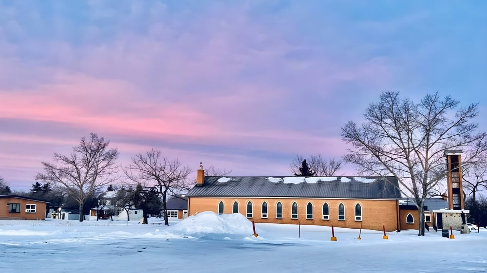 Das Athol Murray College of Notre Dame zeigt ein Backsteingebäude mit verschneitem Winterwald und buntem Himmel im Hintergrund.