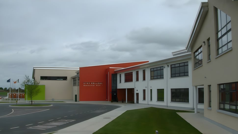 Das moderne mehrstöckige Gebäude mit roter Akzentwand auf dem Campus des Athy College ist von einem gepflasterten Bereich und einer Rasenfläche umgeben.