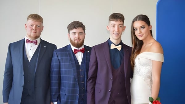 Vier Personen posieren in formeller Kleidung vor blauem Hintergrund auf dem Campus des Athy College.