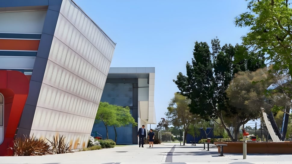 Das moderne Gebäude des Atwell College ist von grünen Anlagen umgeben und steht vor einem klaren blauen Himmel.