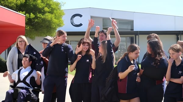 Eine Gruppe von Schülerinnen und Schülern versammelt sich draußen vor einem Gebäude des Atwell College, einige heben die Arme.