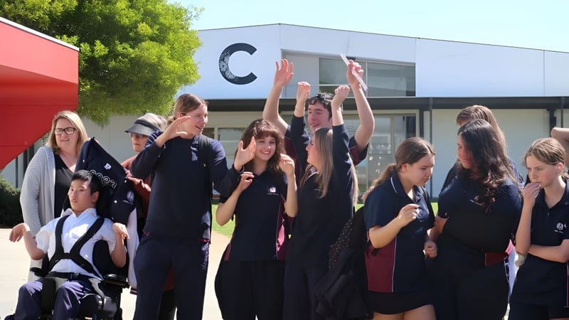 Eine Gruppe von Schülerinnen und Schülern versammelt sich draußen vor einem Gebäude des Atwell College, einige heben die Arme.