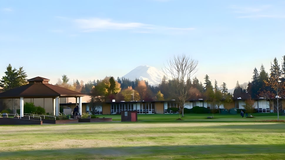 Auf dem Gelände der Auburn Adventist Academy ist ein Pavillon auf einer Wiesenfläche mit Bäumen und schneebedecktem Berg im Hintergrund zu sehen.
