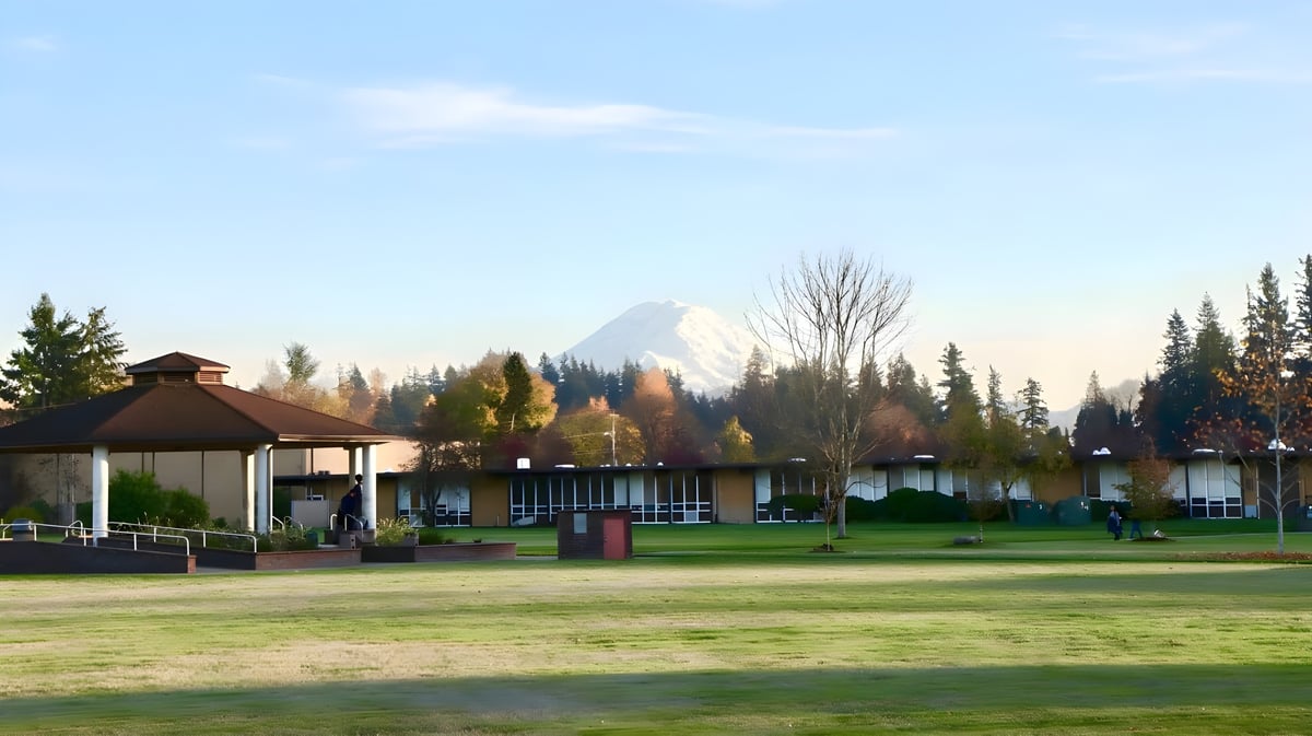 Auf dem Gelände der Auburn Adventist Academy ist ein Pavillon auf einer Wiesenfläche mit Bäumen und schneebedecktem Berg im Hintergrund zu sehen.