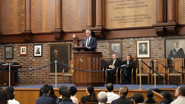 Ein Mann steht am Rednerpult und spricht vor einer großen Zuhörerschaft im prunkvollen Saal der Auckland Grammar School.