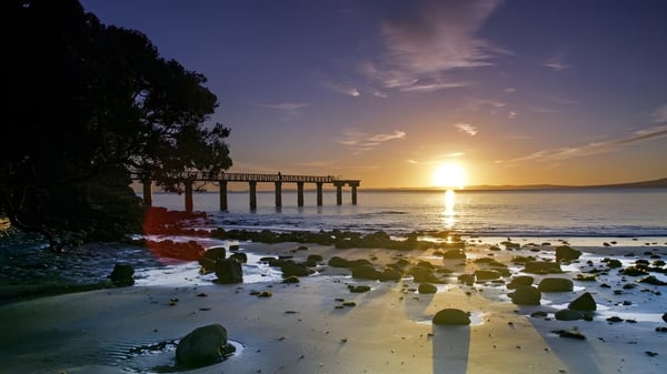 Ein hölzerner Pier erstreckt sich bei Sonnenuntergang in ruhiges Wasser in der Nähe der Auckland Grammar School.