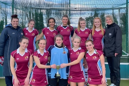 Eine Gruppe junger Sportlerinnen im roten und blauen Trikot posiert auf einem Sportfeld auf dem Gelände der Austin Friars School.