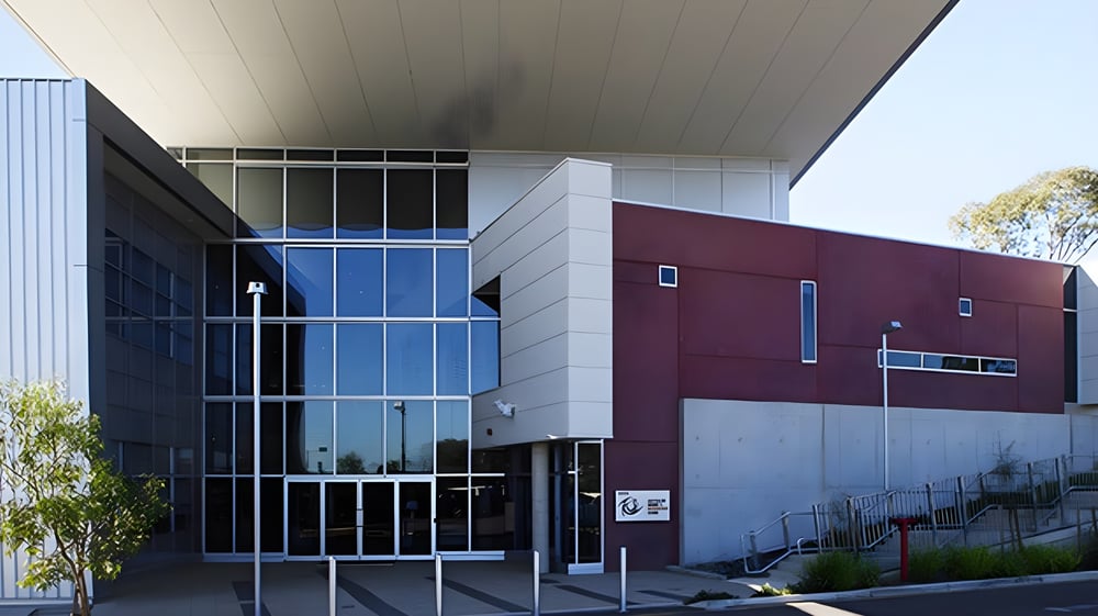 Das moderne Hauptgebäude der Australian Science and Mathematics School mit Glaseingang und Metallgeländer umgeben von Bäumen und einer Rasenfläche.