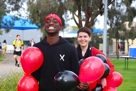Zwei Personen stehen im Park mit roten und schwarzen Luftballons auf dem Campus von Avenues College.