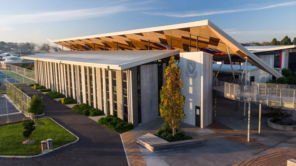 Das moderne Gebäude des Avondale College mit einer markanten Holzdachkonstruktion steht in einer gepflegten Grünanlage.