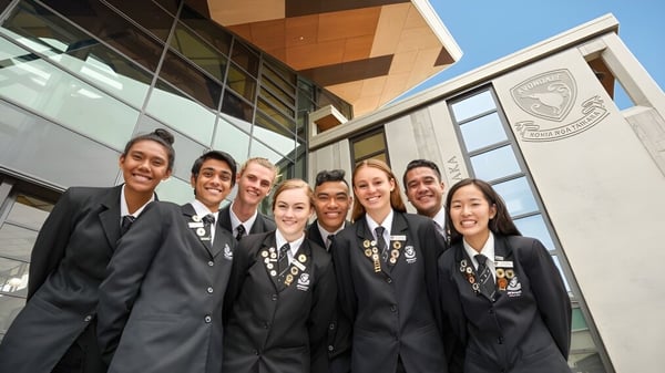 Eine Gruppe von Schülern in formeller akademischer Kleidung steht vor einem Gebäude mit dem Wappen von Avondale College.