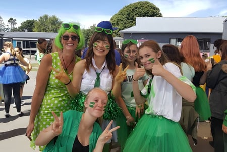 Eine Gruppe Schülerinnen der Avonside Girls' High School posiert vor Gebäuden und Bäumen in grünen und gepunkteten Outfits.