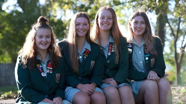 Schülerinnen der Avonside Girls' High School sitzen im Freien zusammen und sind von grüner Natur umgeben.