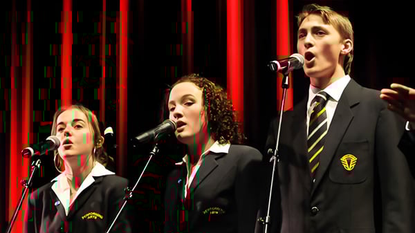 Drei Schülerinnen und Schüler von Awatapu College treten auf der Bühne vor roten Vorhängen auf und singen in Mikrofone.