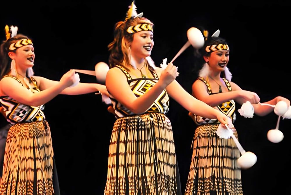 Drei Schülerinnen des Awatapu College führen einen traditionellen ethnischen Tanz auf einer Bühne auf.