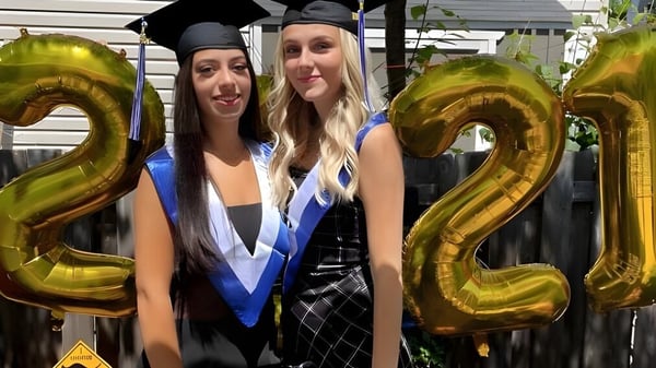 Zwei Schülerinnen der A.Y. Jackson Secondary School posieren in Abschlusskleidung vor goldenen Zahlenballons mit der 