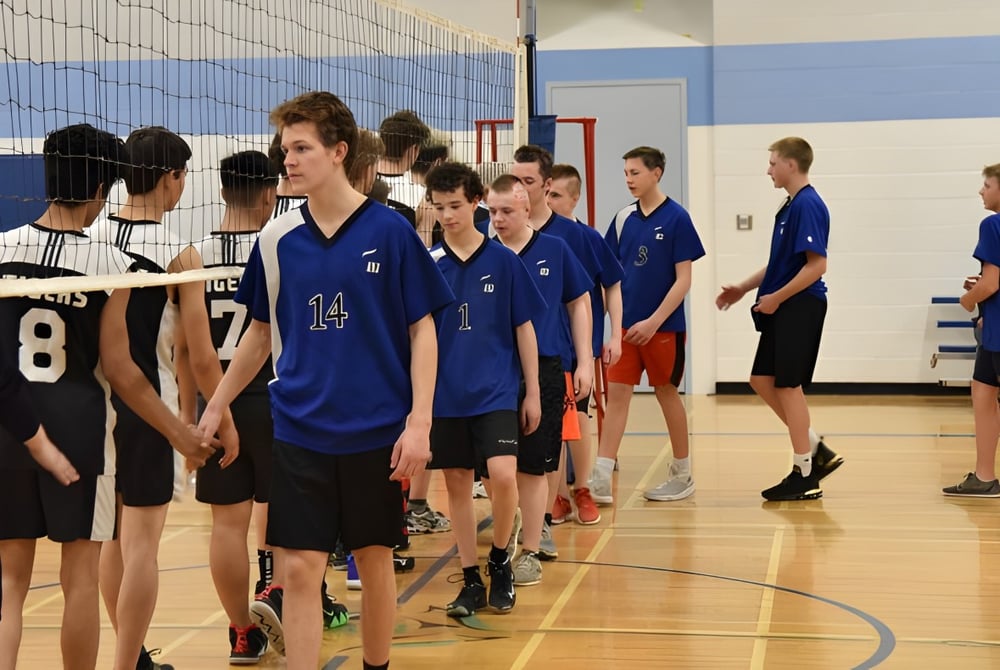 Schüler der A.Y. Jackson Secondary School stehen in blauen und schwarzen Trikots gemeinsam auf dem Basketballfeld in der Turnhalle.