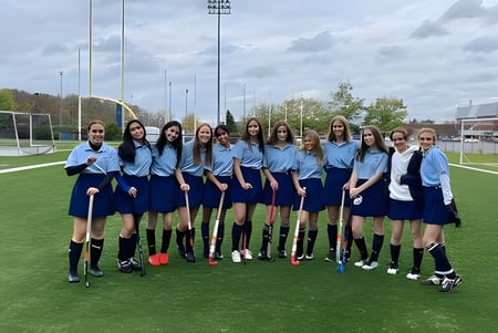 Eine Gruppe Schülerinnen in einheitlichen Trikots steht auf dem Fußballfeld der A.Y. Jackson Secondary School mit der Stadtkulisse im Hintergrund.
