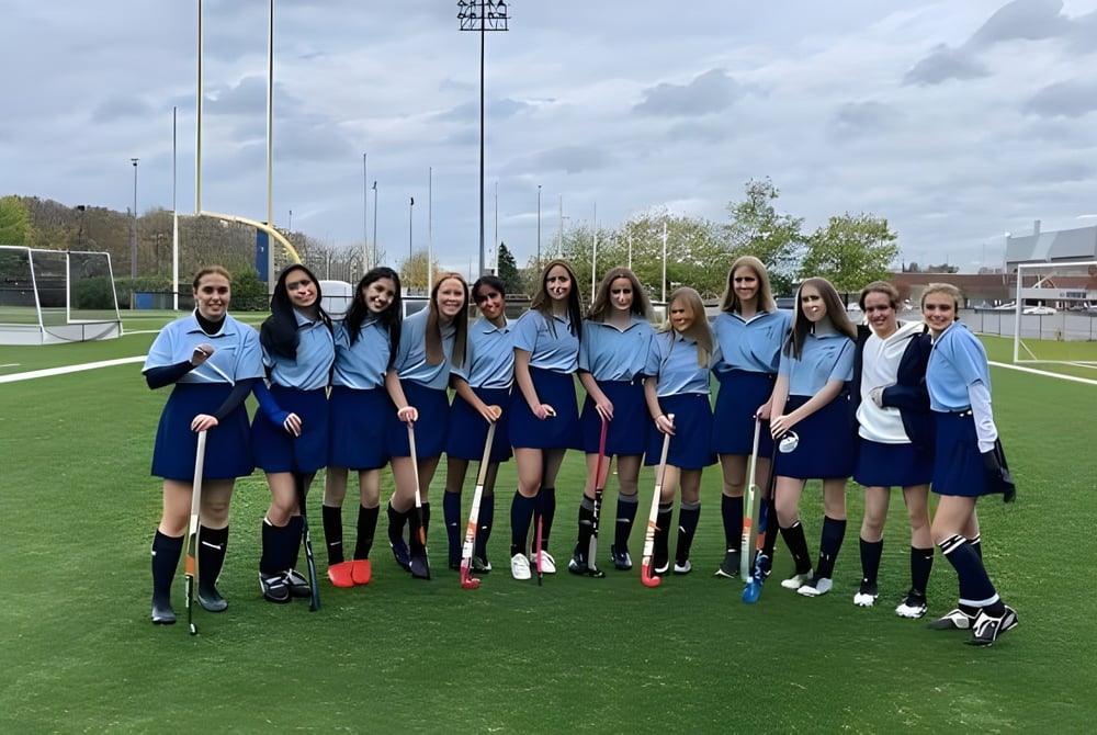 Eine Gruppe Schülerinnen in einheitlichen Trikots steht auf dem Fußballfeld der A.Y. Jackson Secondary School mit der Stadtkulisse im Hintergrund.