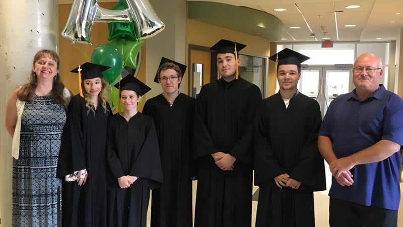 Eine Gruppe von Schülerinnen und Schülern der A.Y. Jackson Secondary School steht in Abschlussroben und Hüten im Flur mit Luftballons und Dekoration.