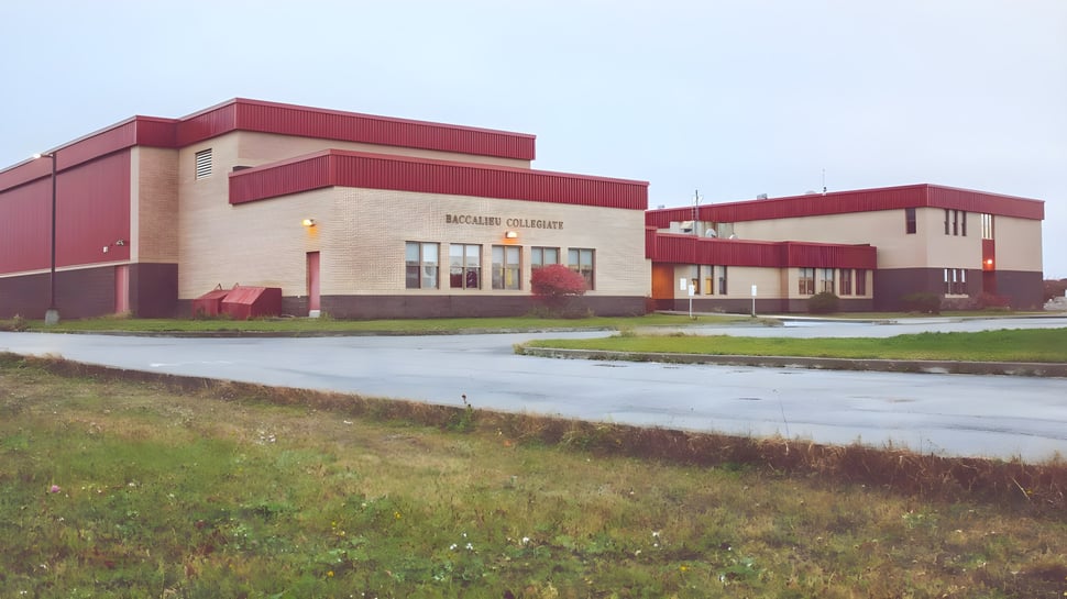 Ein grosses rot-weisses Industriegebäude mit einer Grasfläche im Vordergrund auf dem Gelände des Baccalieu Collegiate.