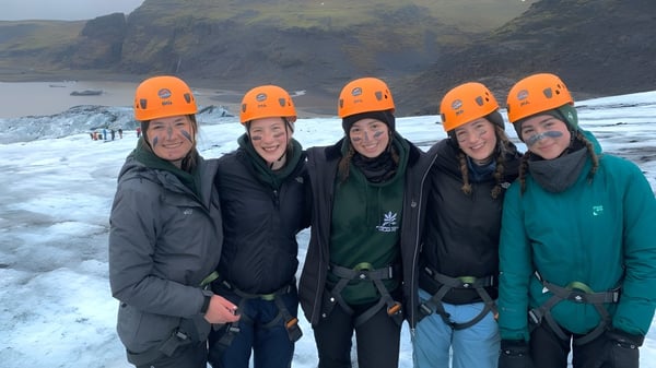 Eine Gruppe von Schülerinnen und Schülern der Badminton School steht in orangenen Schutzhelmen in einer verschneiten Berglandschaft.