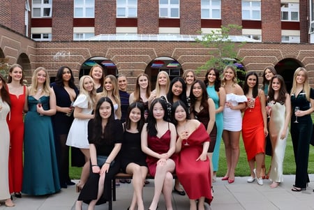 Eine Gruppe junger Frauen in formeller Kleidung steht vor einem Backsteingebäude mit Bogenfenstern auf dem Gelände der Badminton School.