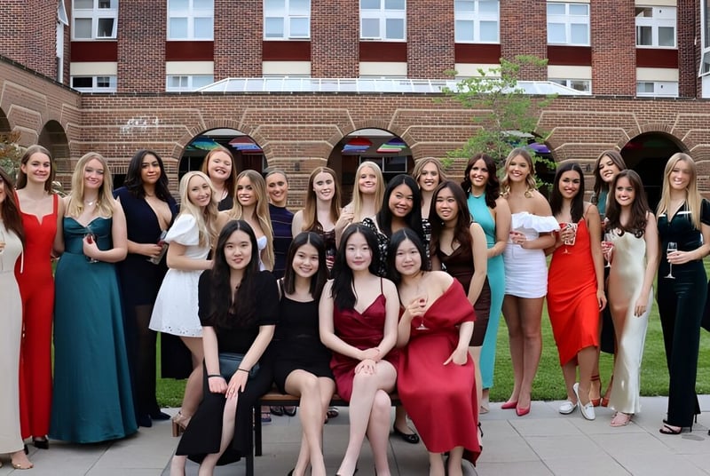 Eine Gruppe junger Frauen in formeller Kleidung steht vor einem Backsteingebäude mit Bogenfenstern auf dem Gelände der Badminton School.