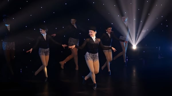 Schüler der Badminton School führen auf einer Bühne mit Sternenhintergrund in formeller Kleidung einen Tanz vor.