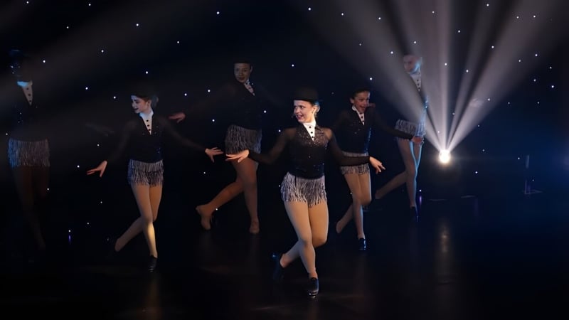 Schüler der Badminton School führen auf einer Bühne mit Sternenhintergrund in formeller Kleidung einen Tanz vor.