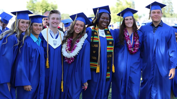 Eine Gruppe von Absolventen in blauen Talaren steht draußen im Grünen auf dem Campus der Bakersfield Christian.