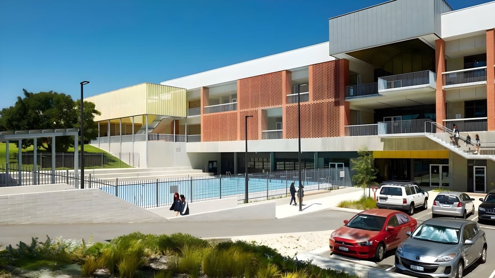 Das mehrstöckige Gebäude der Balcatta Senior High School mit einem Schwimmbecken im Vordergrund und parkenden Autos ist von viel Grün umgeben.