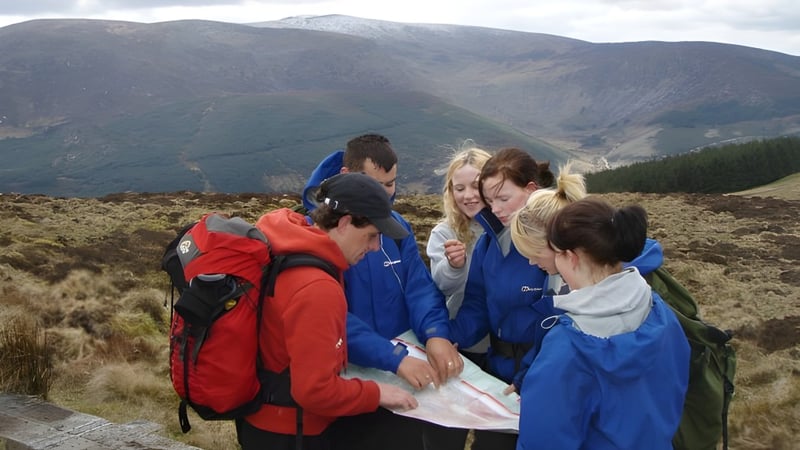 Eine Gruppe Schülerinnen und Schüler der Balla Secondary School steht in Bergbekleidung in einer bergigen Landschaft unter bewölktem Himmel.