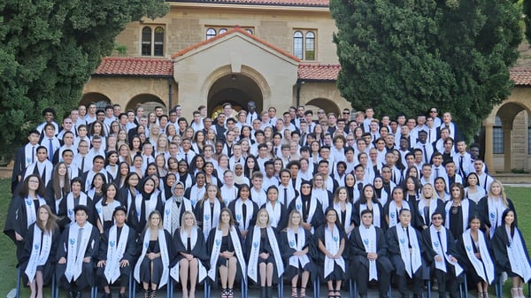 Eine Gruppe von Schülern in Abschlusskleidung steht vor einem historischen Gebäude auf dem Campus des Ballajura Community College.