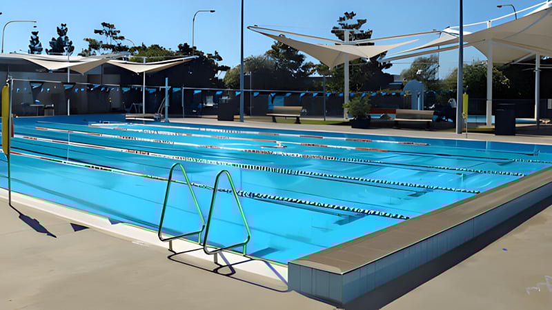 Das große Schwimmbecken im Außenbereich des Ballajura Community College ist von schattigen Sitzbereichen und Bäumen umgeben.
