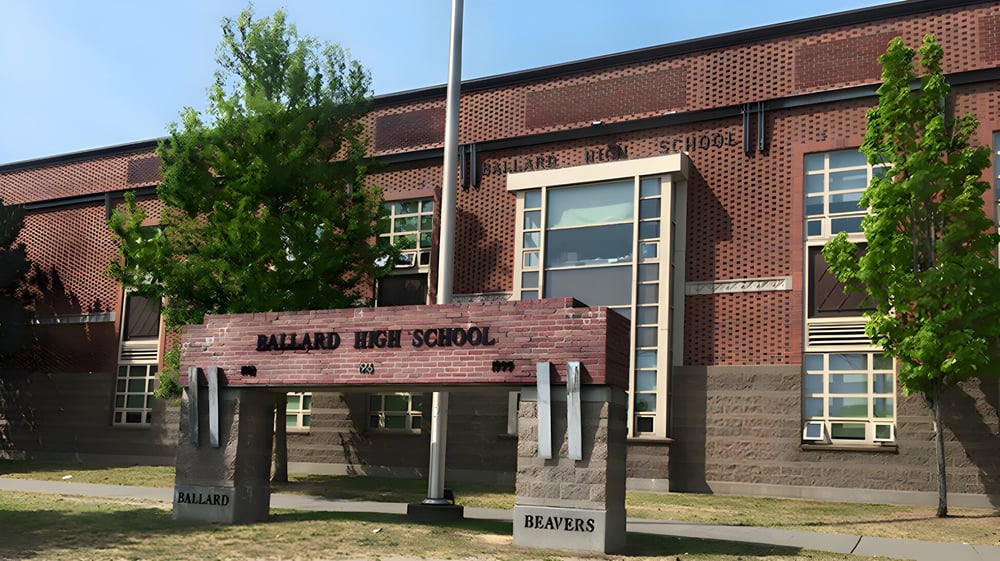 Das Backsteingebäude der Ballard High School ist von Bäumen und Laternen im Vordergrund umgeben.